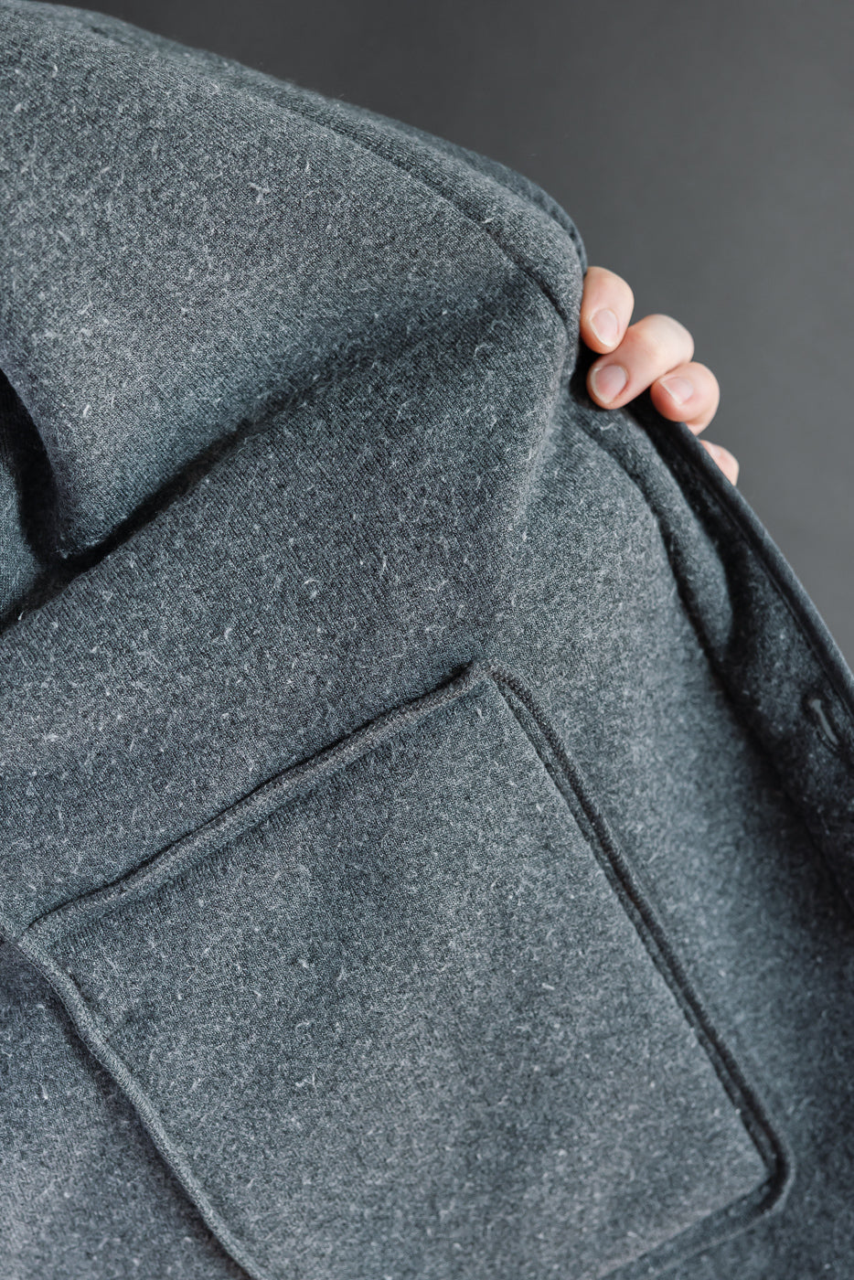Close-up of the back of a grey wool coat showing fabric texture and a large patch pocket.