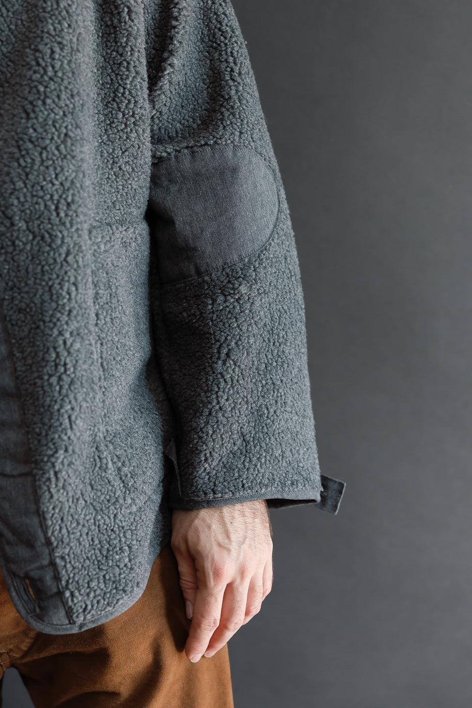 Close-up side view of a male model's grey sherpa fleece jacket sleeve with elbow patch.