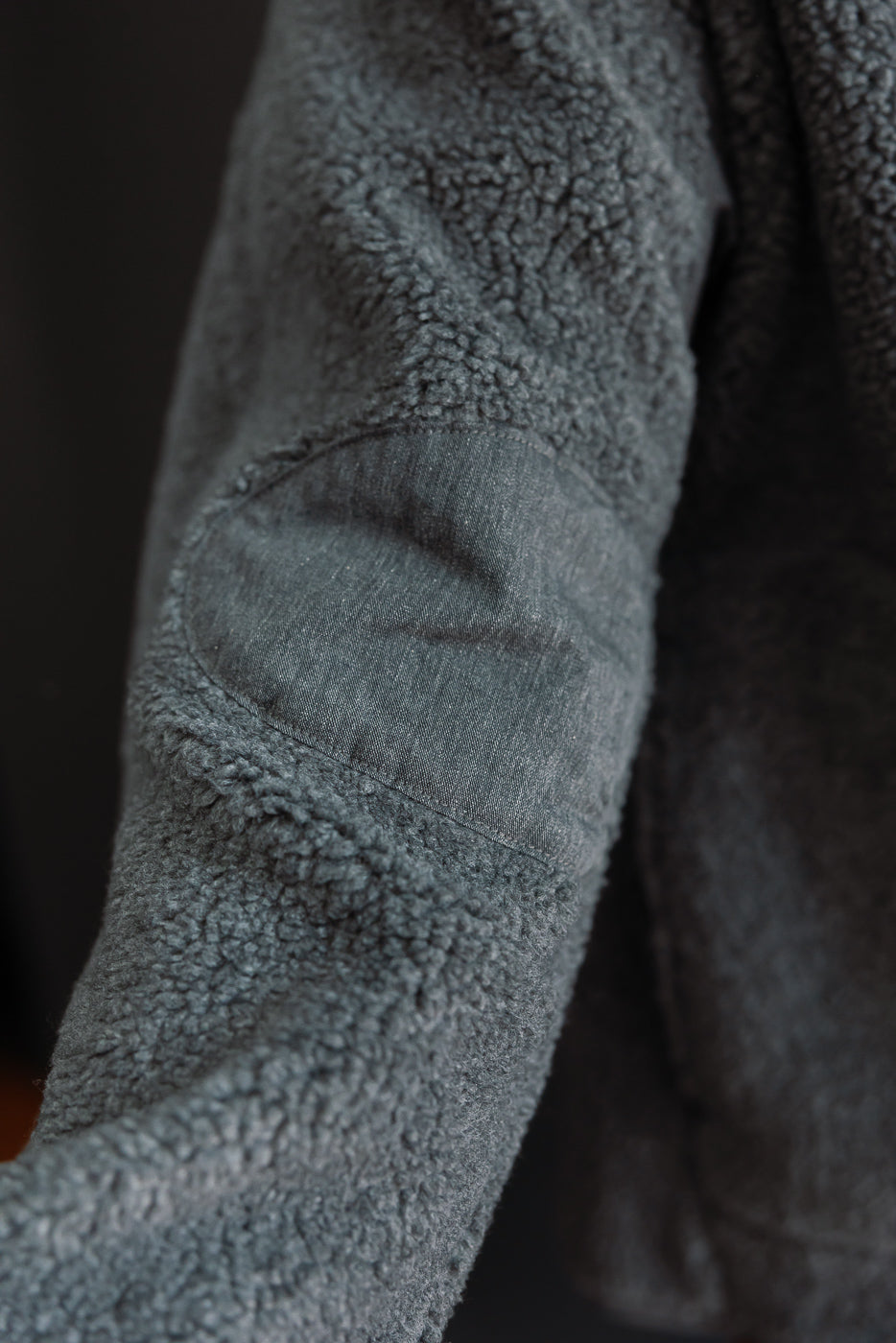 Close-up of a male model's grey sherpa fleece sleeve showing a woven elbow patch detail.