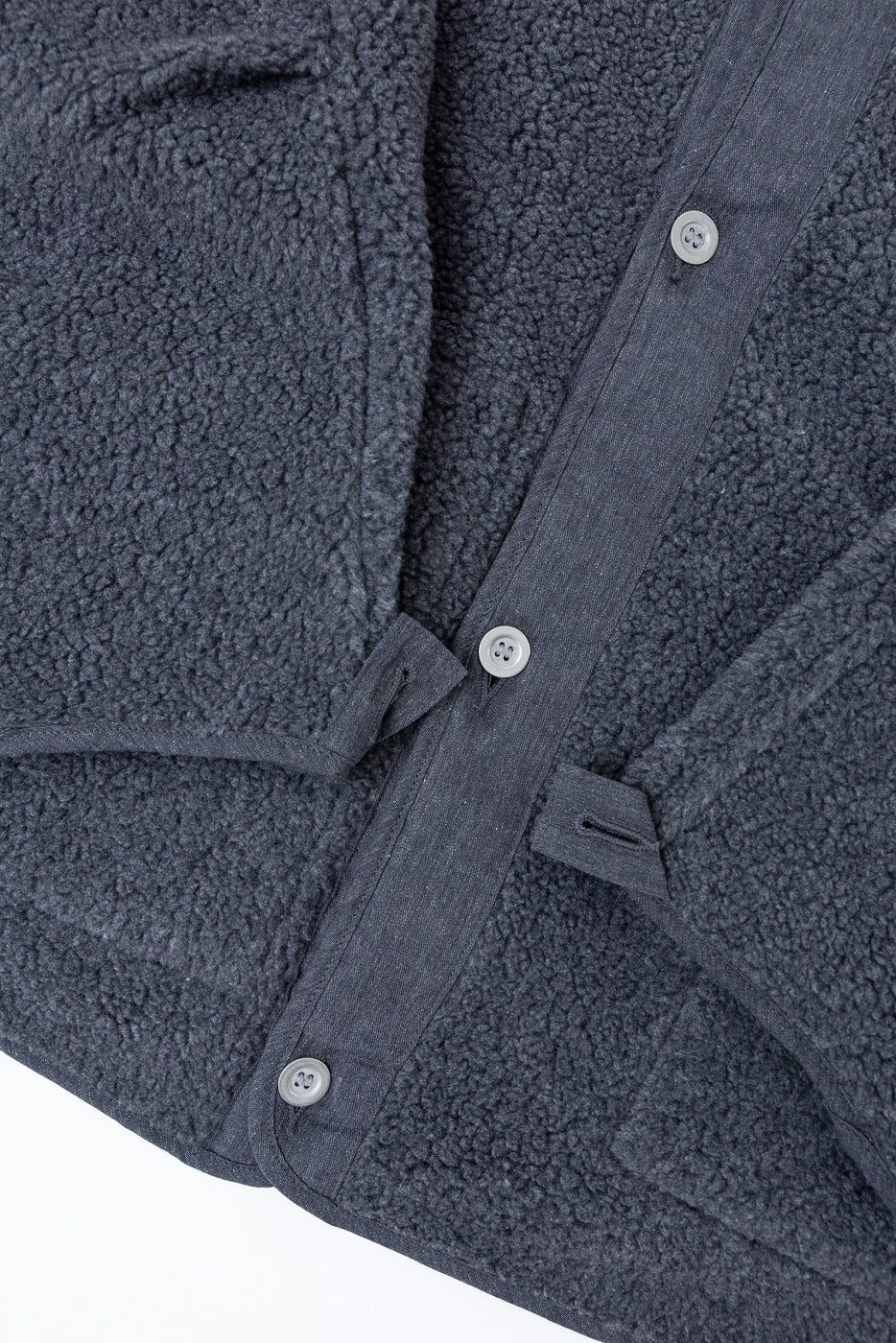 Close-up of the front of a dark grey textured fleece shirt showing buttons and fabric.