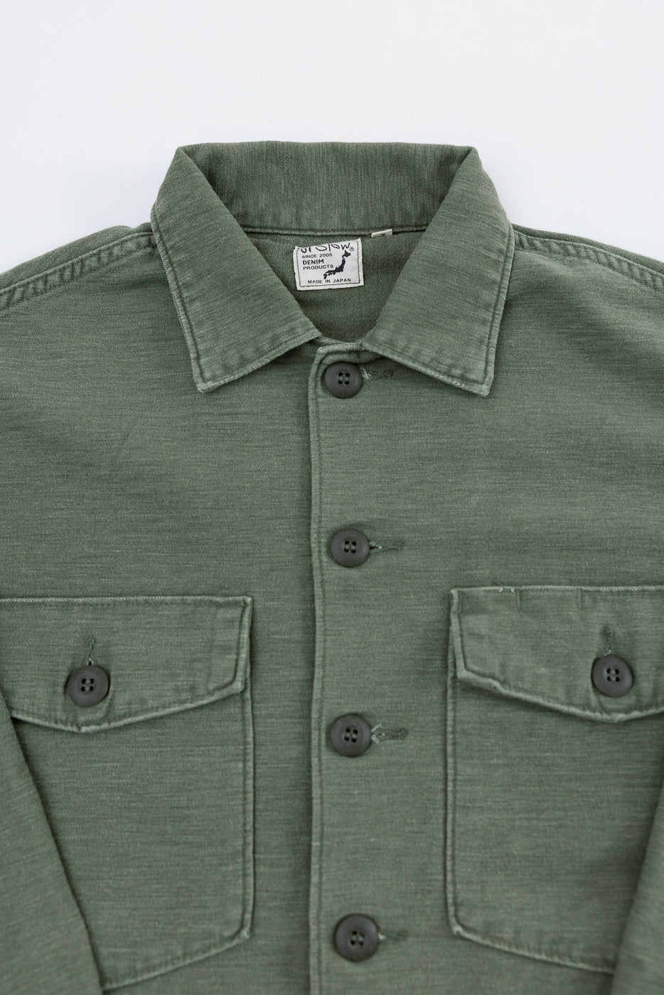 Close-up of orSlow dark olive reverse sateen fatigue shirt front, highlighting buttons, collar, chest pockets, and fabric texture, at Dant Indianapolis.