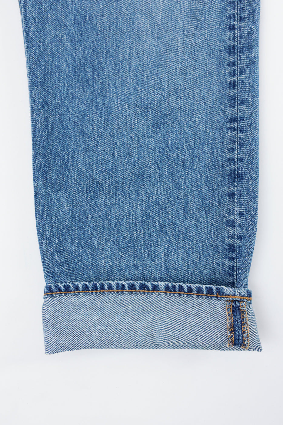Close-up of the bottom hem and cuffed leg of blue denim jeans, showing fabric texture and stitching.