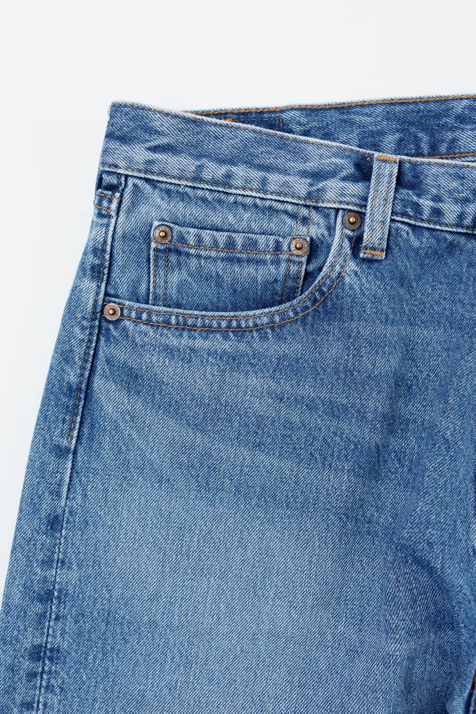 Close-up of the front waistband and pocket area of blue denim jeans showing fabric texture.