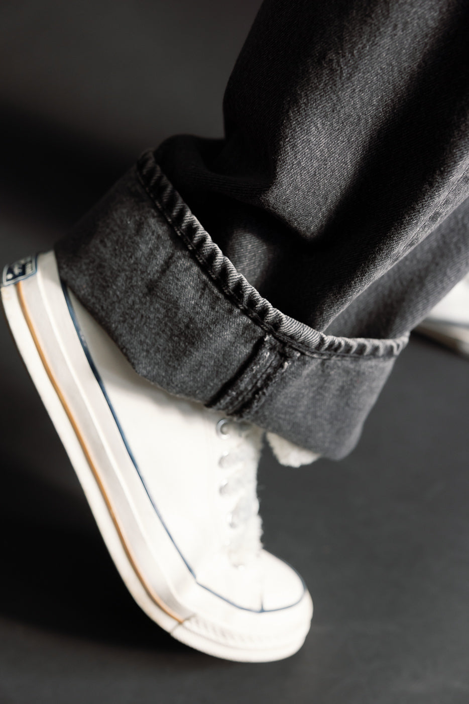 Close-up of male model’s cuffed hem orSlow Super Dads Fit black denim jeans with visible texture, paired with white sneakers.