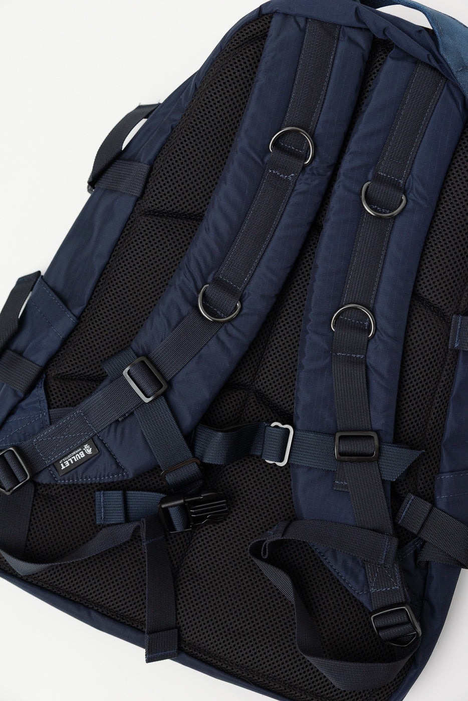 Close-up of navy nylon ripstop backpack back panel showing adjustable padded straps, mesh padding, and metal D-rings.