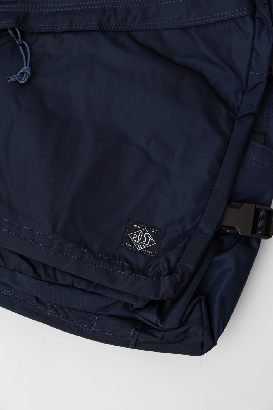 Close-up of navy nylon ripstop Post O'Alls bag, front lower corner with logo tag detail.