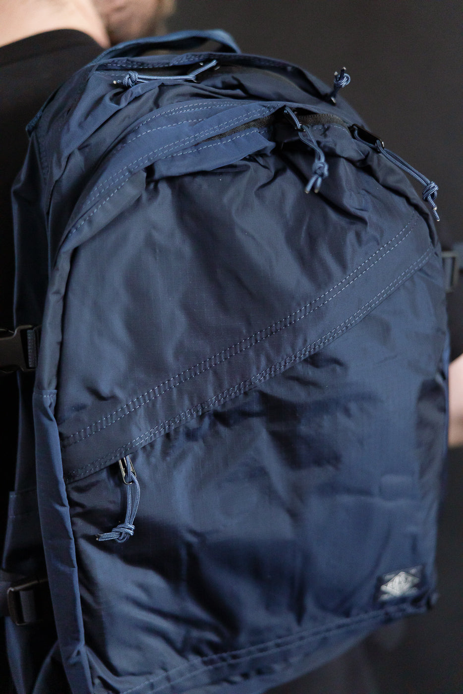 Close-up of navy nylon ripstop backpack front, worn by male model, focusing on zipper details