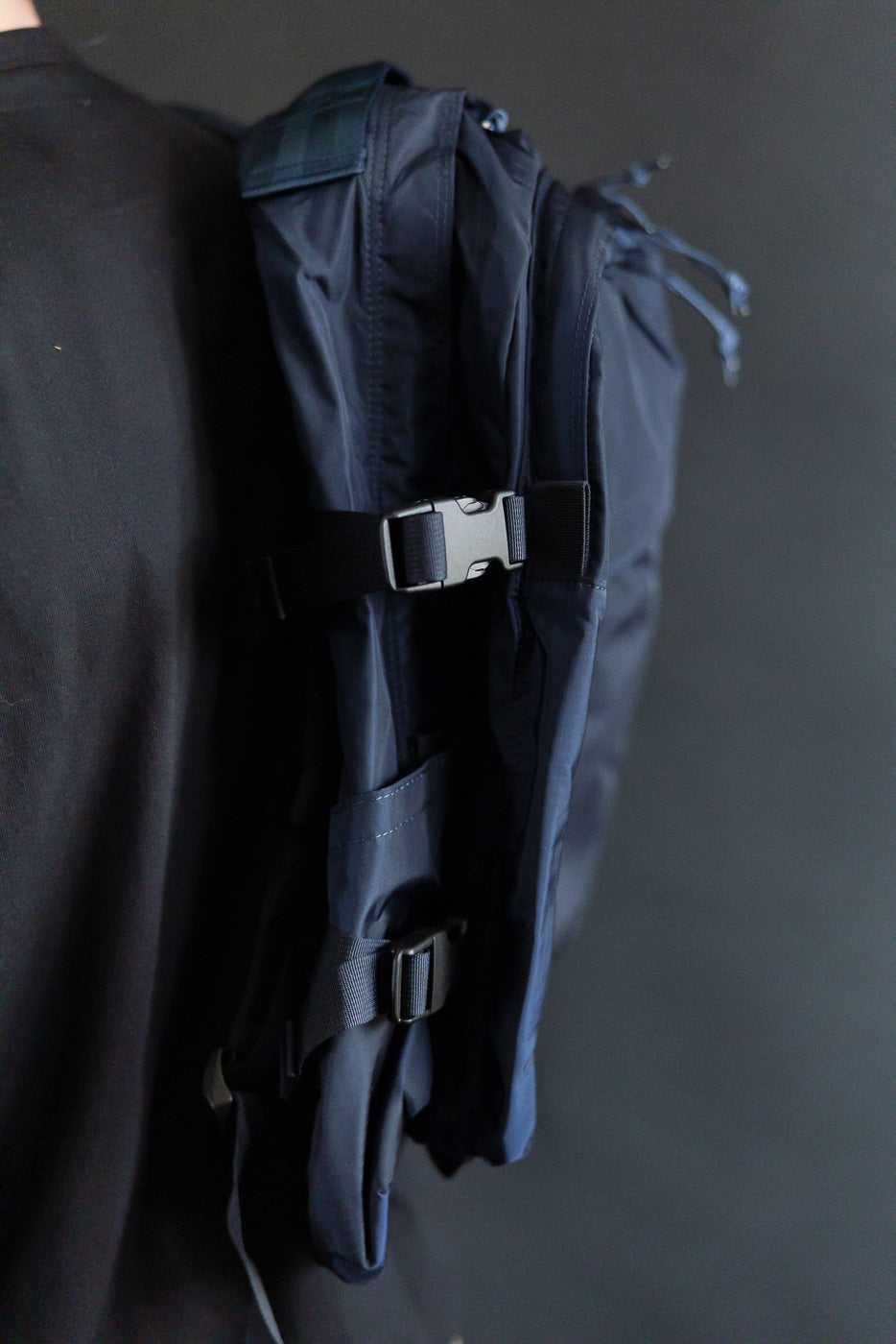 Close-up side view of navy nylon ripstop backpack on male model, showing straps and buckle detail