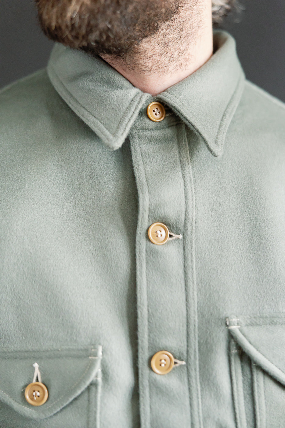 Close-up front detail of pale green wool jacket, pointed collar, tan buttons, chest pockets, on male model 5'9