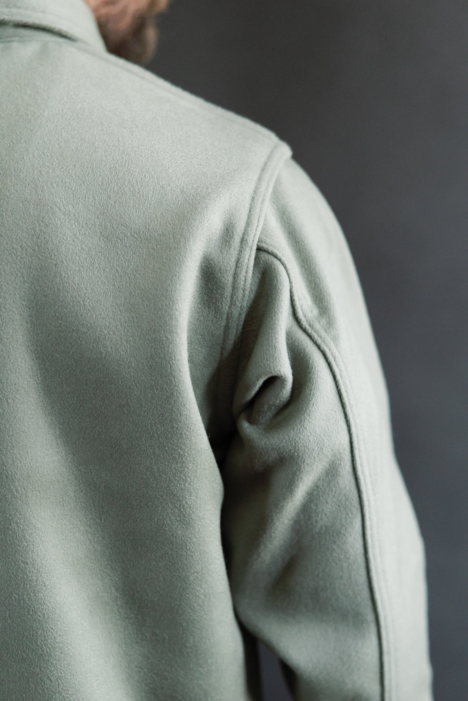 Close-up of back left shoulder and sleeve seam on pale green melton jacket, textured fabric, male model 5'9 165lbs athletic build, Dant contemporary casual apparel.