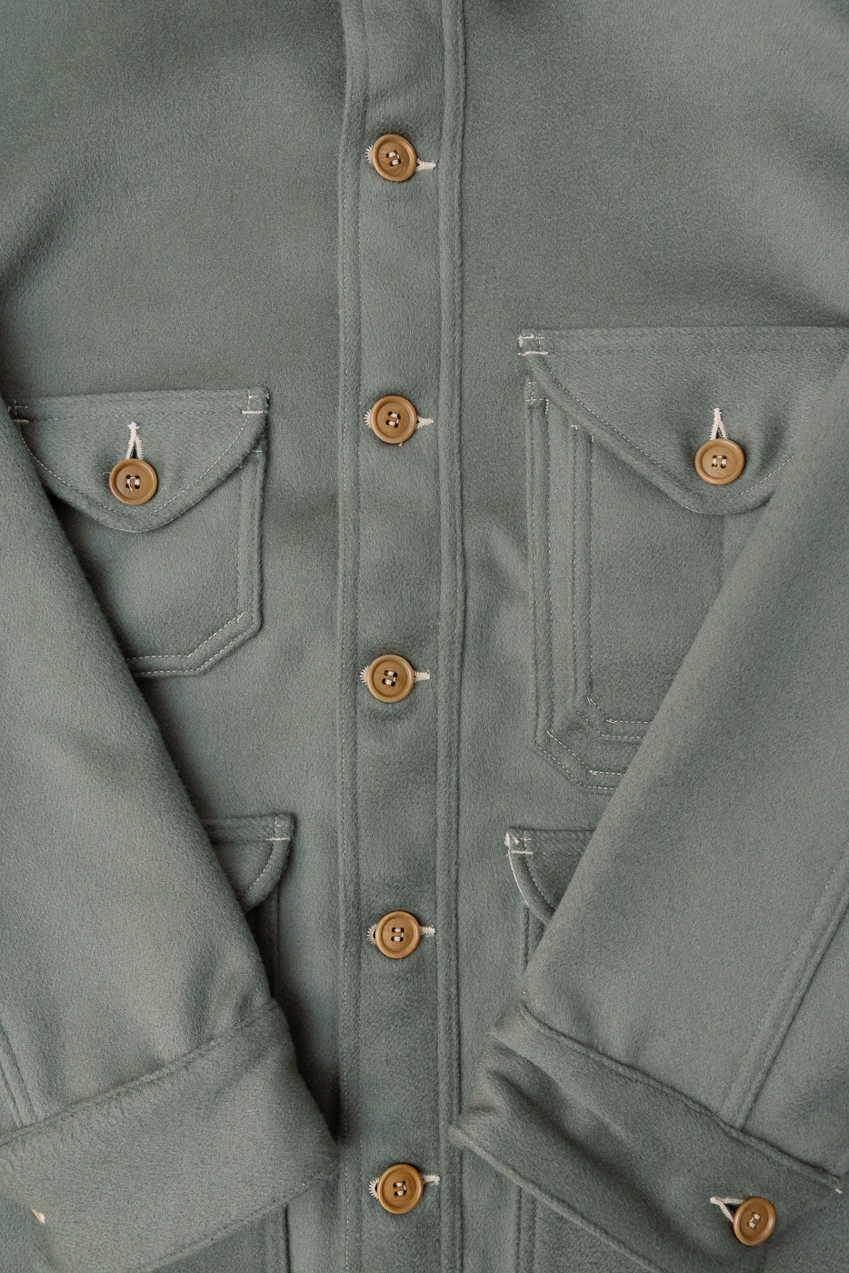 Close-up of front of pale green melton jacket, showing buttons, flap pockets, fabric texture