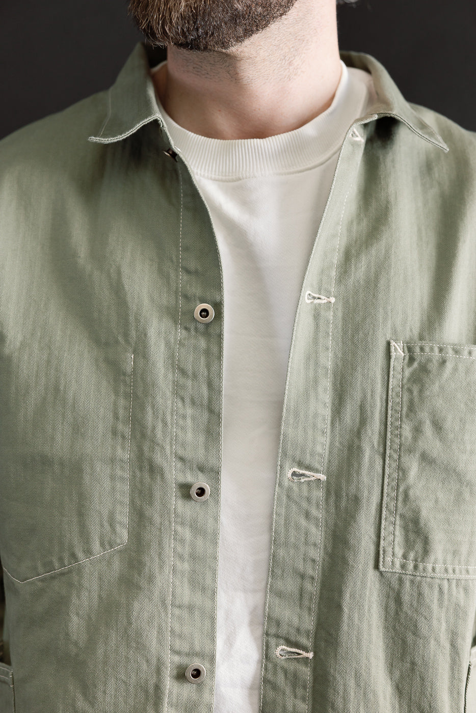Close-up front view of sage green utility jacket collar, chest pocket, and buttons on male model, 5'9