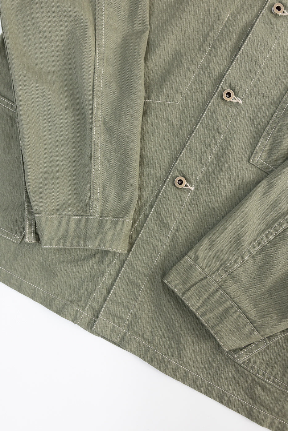 Close-up of sage green utility jacket front, showing herringbone fabric, buttons, cuff, and stitching.