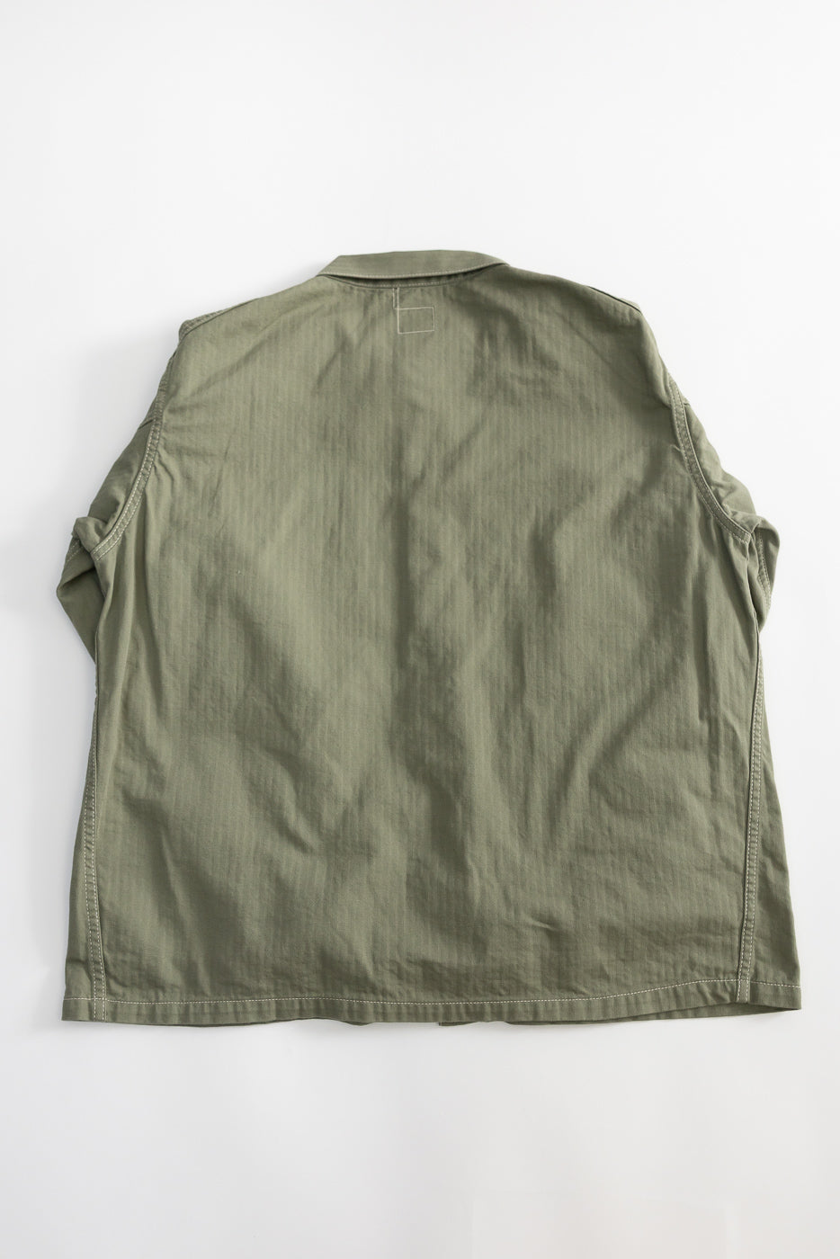 Flat lay of sage green utility jacket, back view showing straight hem and stitched panels.