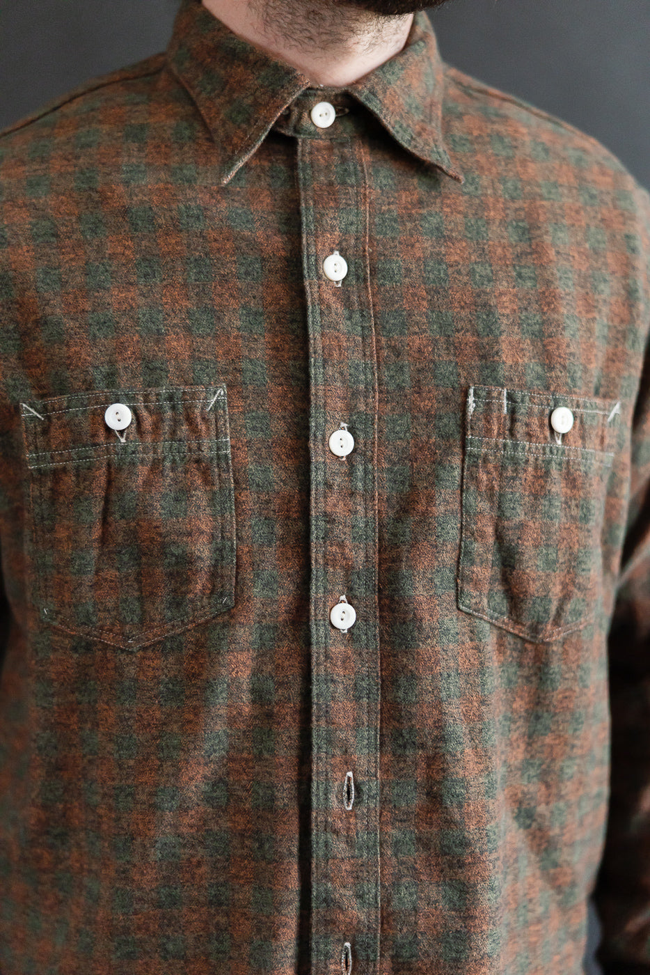 Close-up front view of men's plaid cotton flannel shirt in orange and green, showing chest pockets, buttons, and collar on male model, 5'9