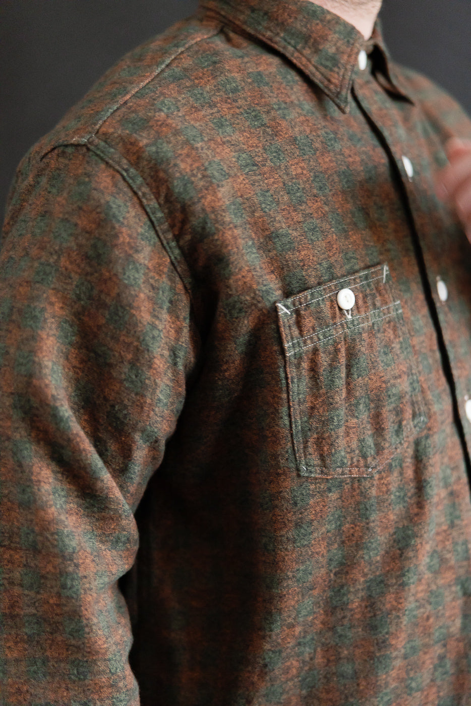 Close-up of male model, 5'9”, 165lbs, athletic build, wearing orange and green plaid flannel shirt, focusing on front left chest pocket and button-down collar.