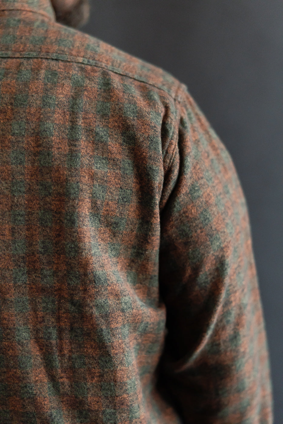 Close-up of back shoulder of Post O'Alls St. Louis orange plaid cotton flannel shirt on male model, showing fabric texture and pattern.