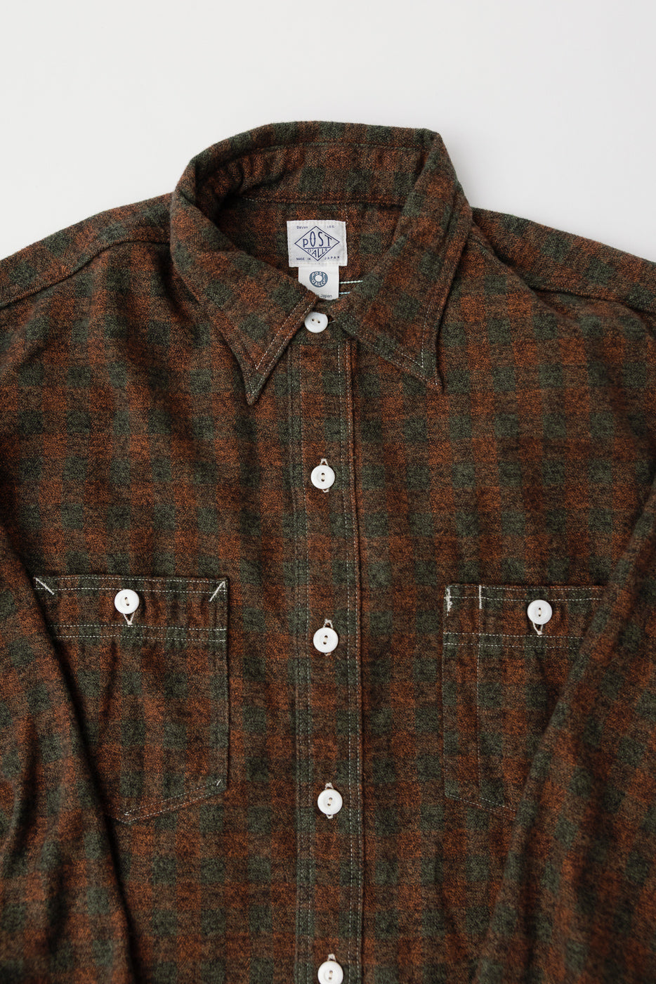 Close-up front of Post O’Alls St. Louis cotton flannel plaid shirt in orange and olive with button-down collar, white buttons, and dual chest pockets, fabric detail visible.