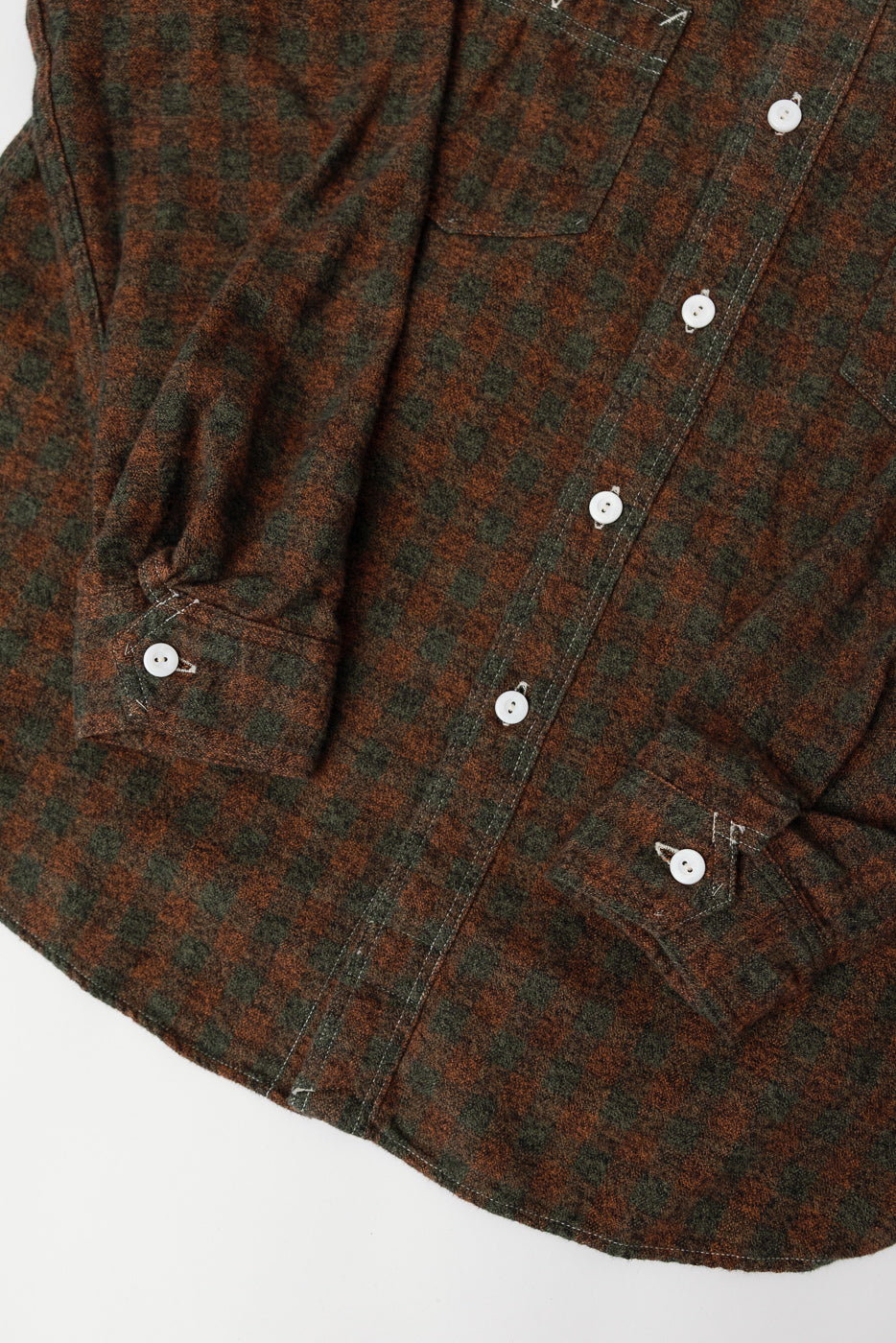 Close-up of front lower section of orange and green plaid cotton flannel shirt, showing button and cuff details.
