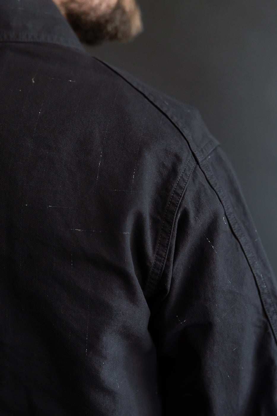 Close-up of male model’s back shoulder in Post O'Alls black nep twill coverall, highlighting fabric texture and stitching detail.