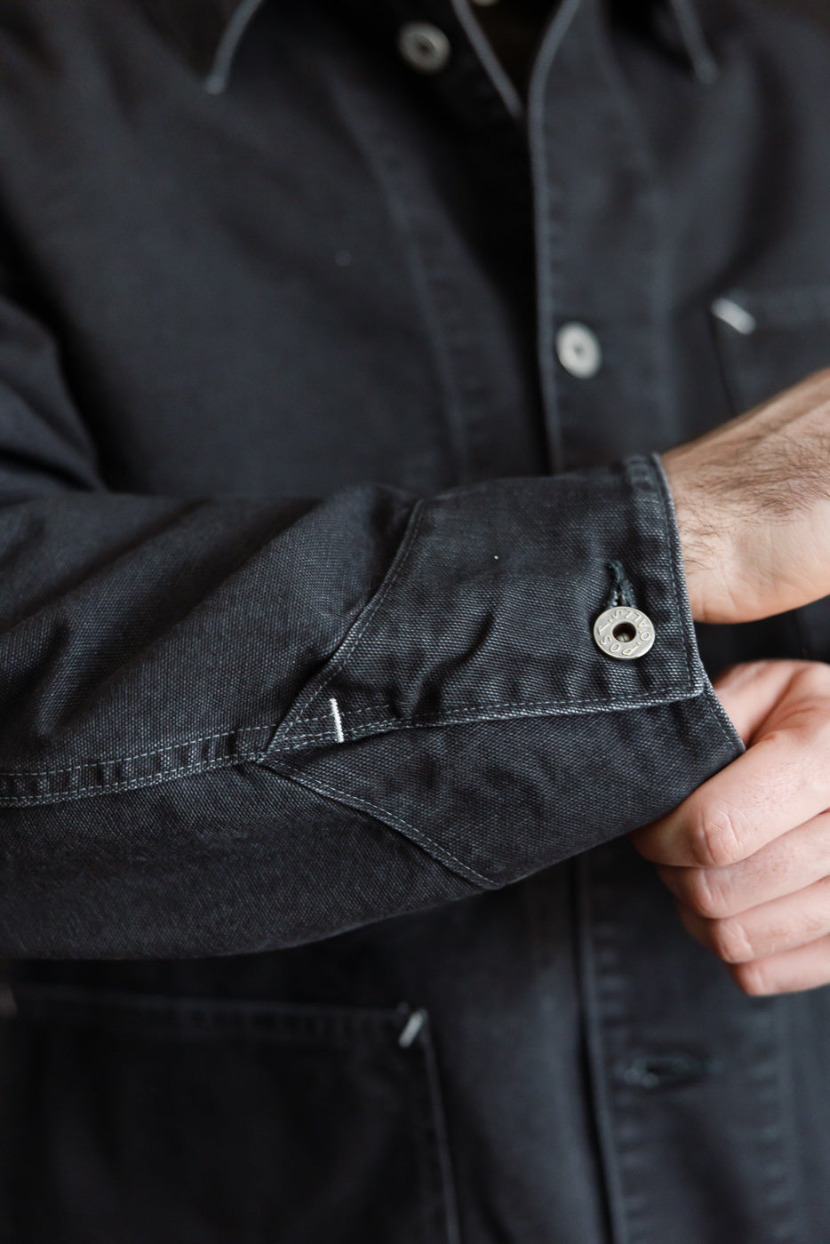 Close-up of washed black pigment-dyed canvas coverall, showing sleeve cuff button detail on male model, 5'9