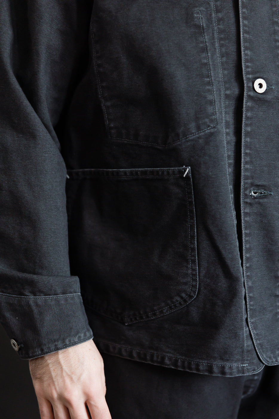 Close-up of front left pocket and sleeve cuff on washed black pigment-dyed canvas coverall, shown on a male model, 5'9