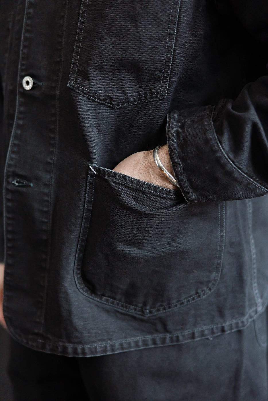 Close-up front view of washed black pigment-dyed canvas coverall pocket on male model, 5'9