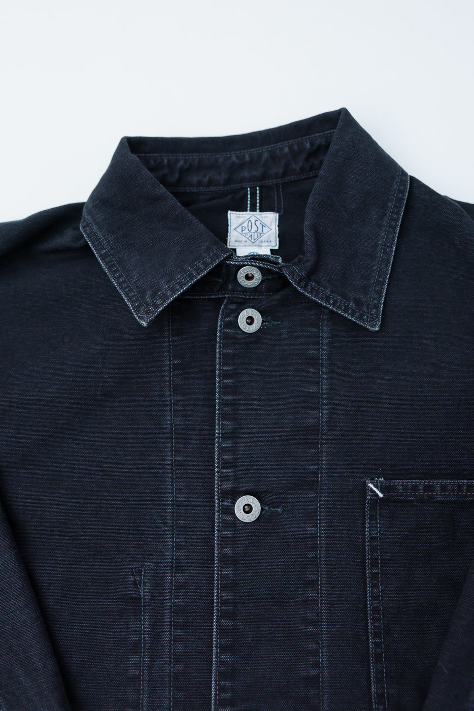 Close-up front view of Post O’Alls black washed canvas coverall chest, showing collar, buttons, pocket, and fabric texture