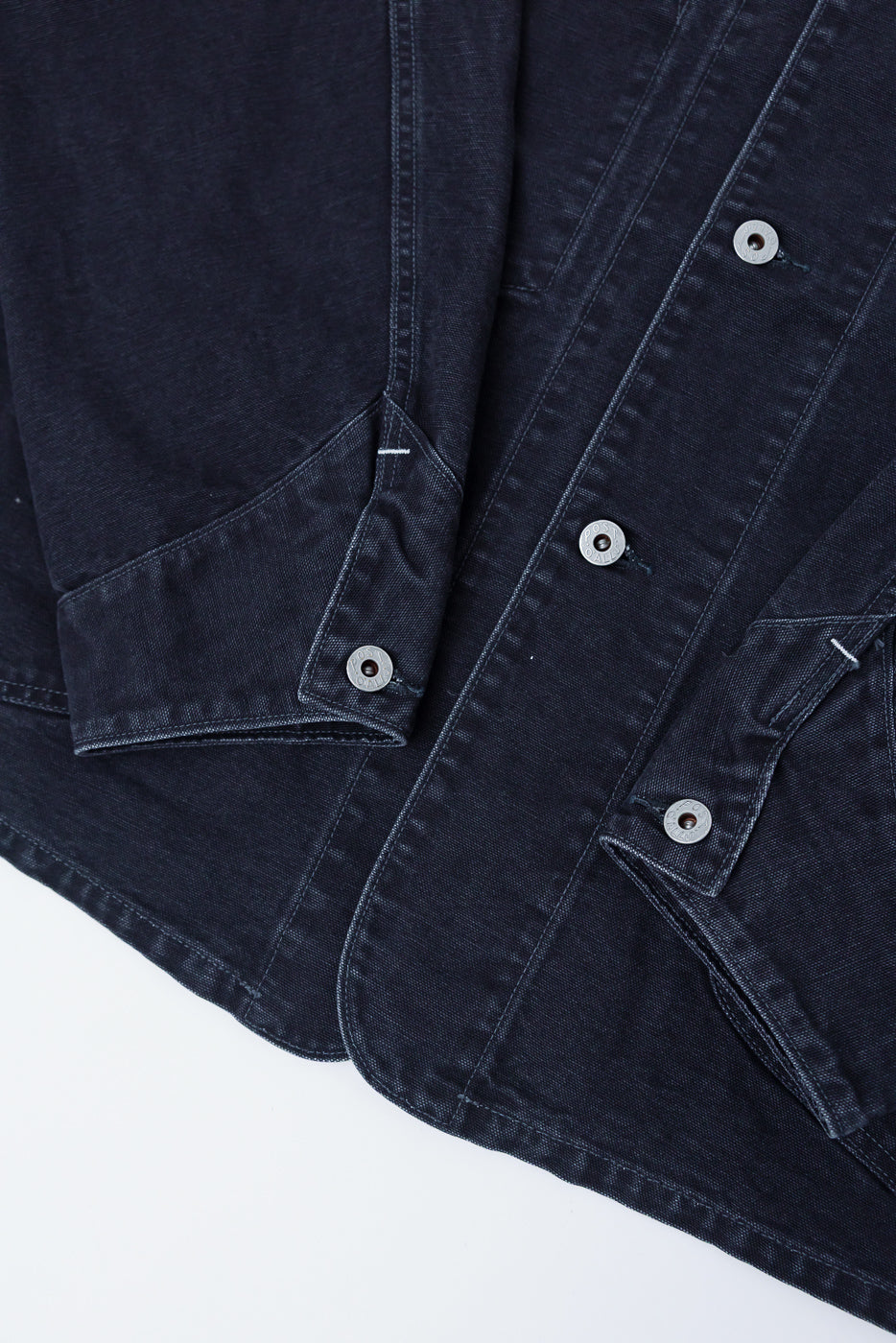 Close-up of washed black pigment-dyed canvas coverall front, showing buttons and large pockets, Dant contemporary casual apparel.