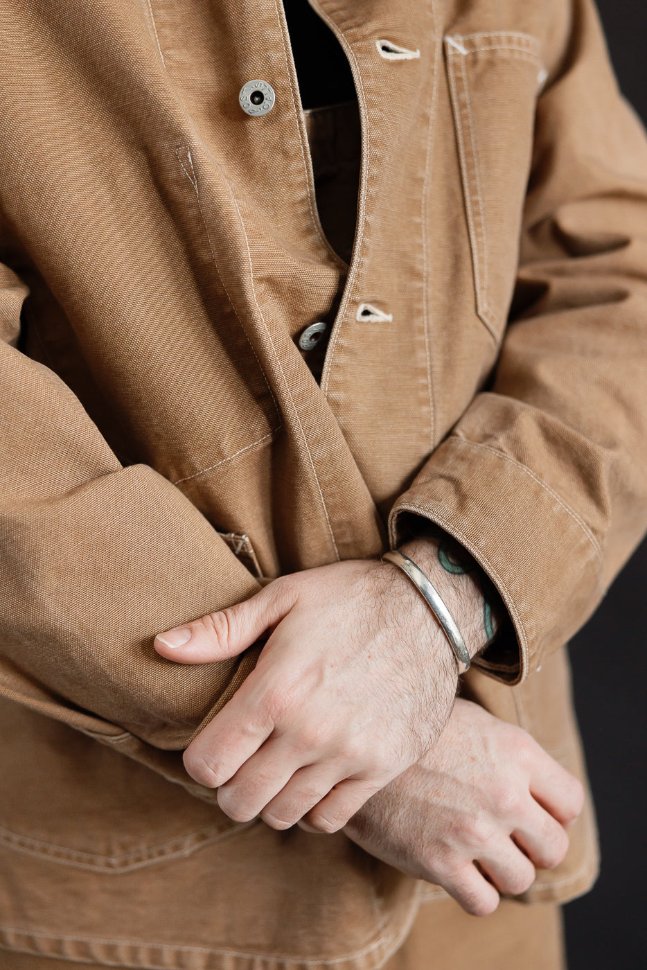 Close-up of male model's torso in brown washed canvas coverall, front view, showing snap buttons and chest pocket detail. Model is 5'9