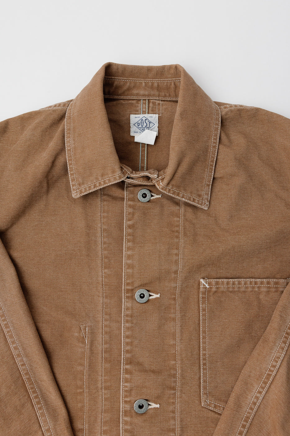 Close-up front view of POST O'ALLS pigment dyed brown canvas coverall, detailing buttons, collar, and chest pocket.