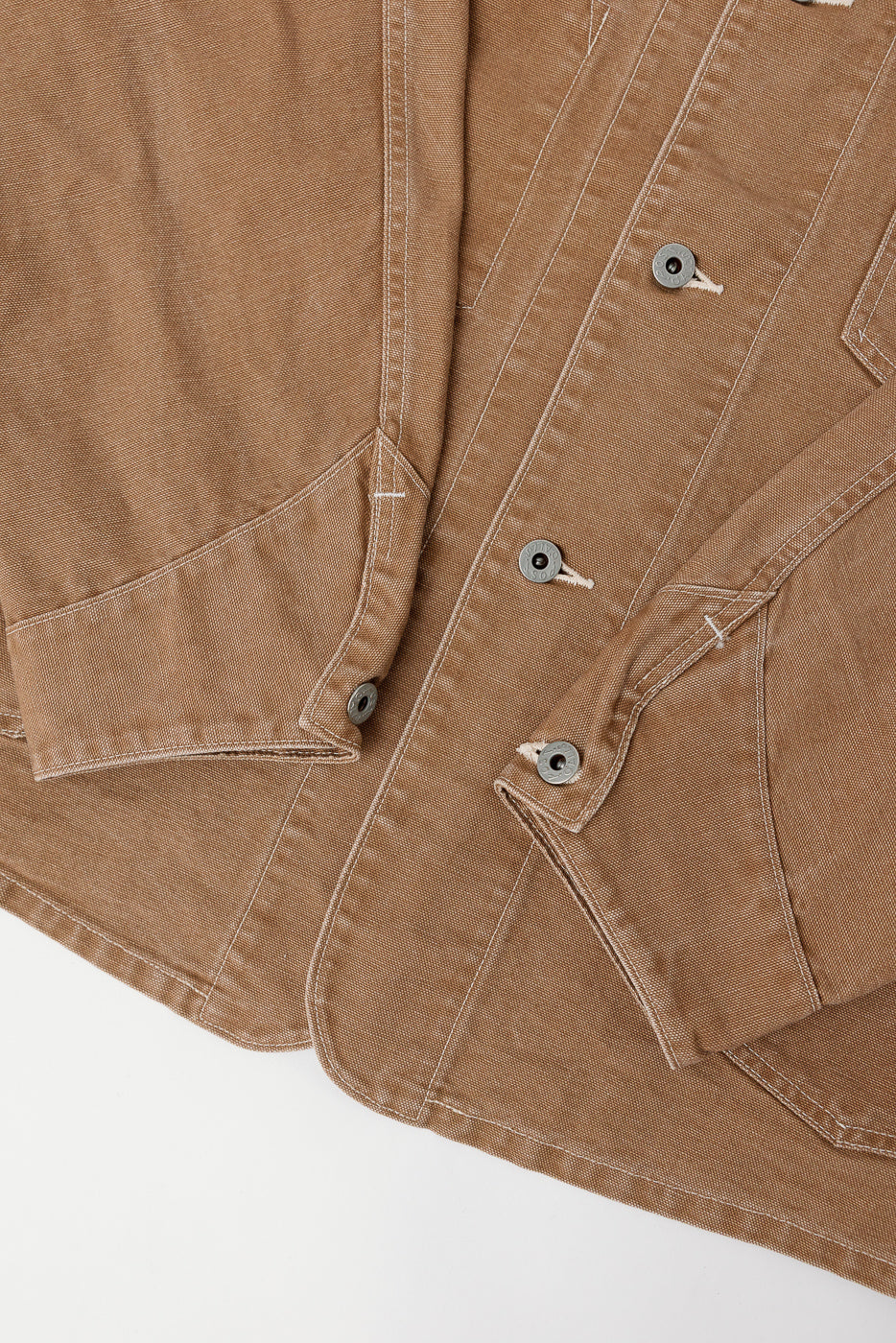 Close-up of brown pigment dyed canvas coverall front, showing button details and pocket stitching.