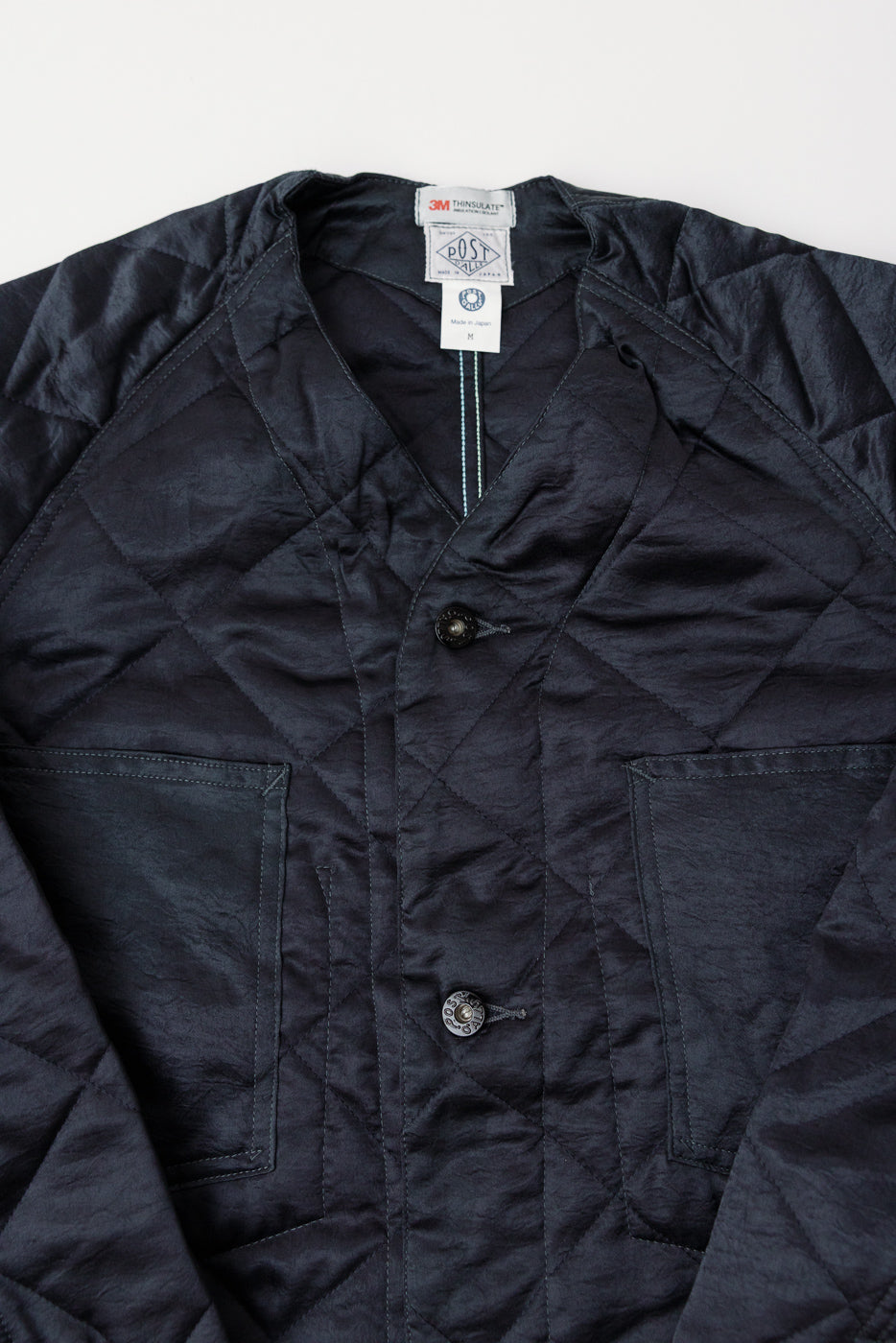 Close-up front of dark grey quilted acetate sateen coverall showing buttons, collar, pockets, and texture.