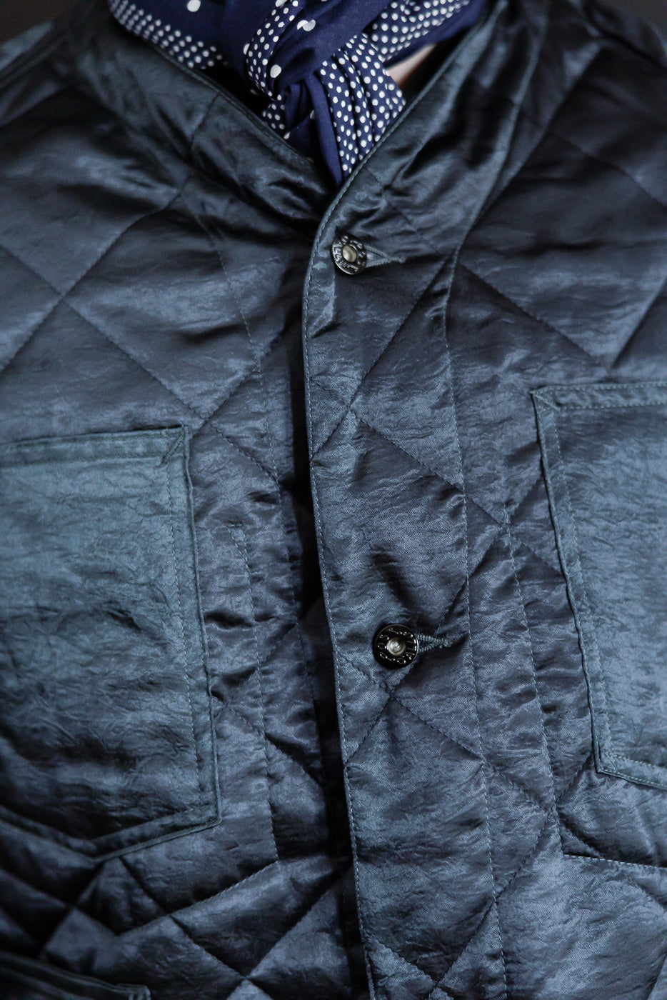 Close-up of male model wearing Post 47 quilted acetate sateen coverall in dark grey, front chest pockets, diamond quilting, and front buttons visible, Dant contemporary casual apparel.