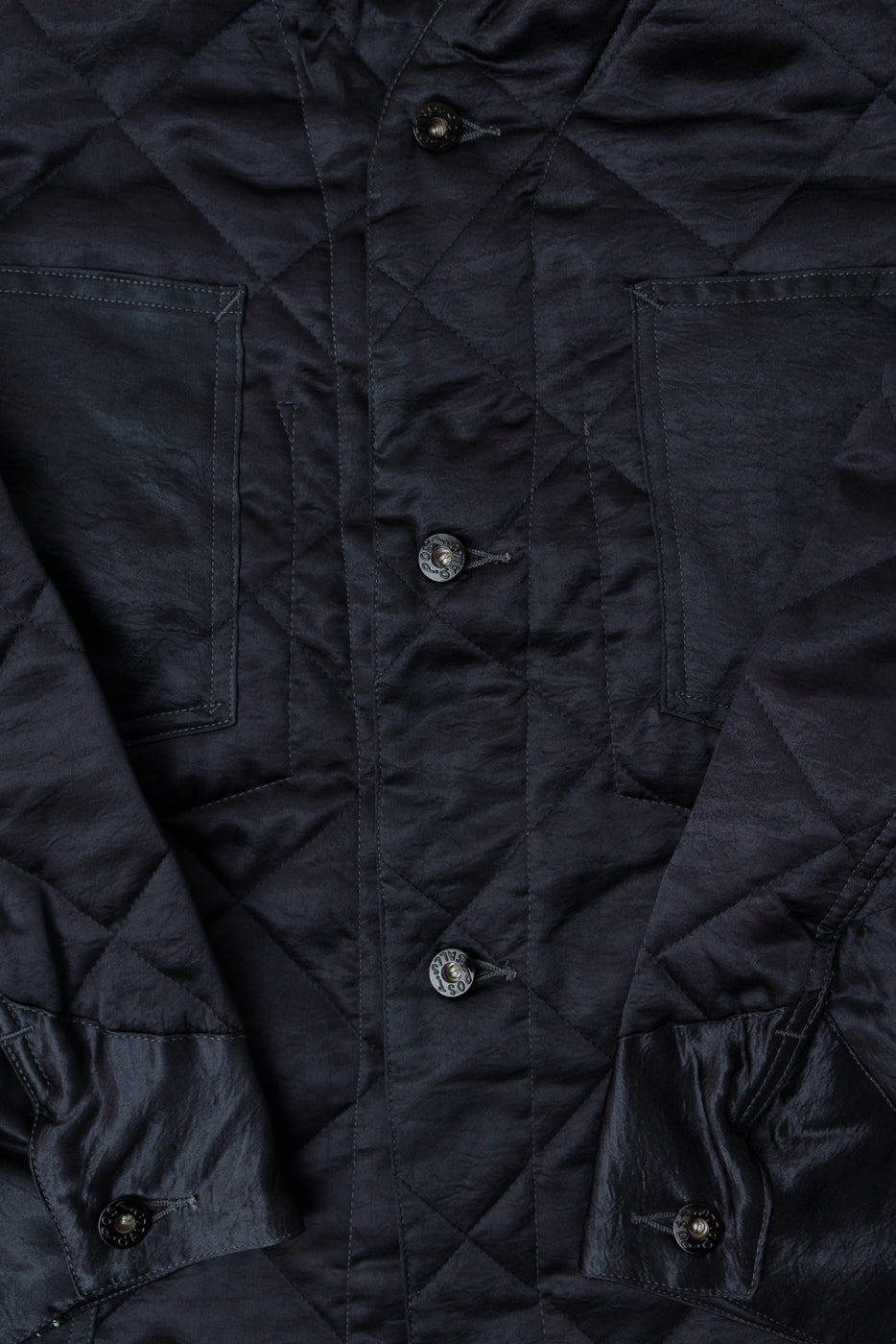 Close-up front view of Post Overalls dark grey quilted acetate sateen coverall, showing buttons, pocket, and diamond stitch texture.