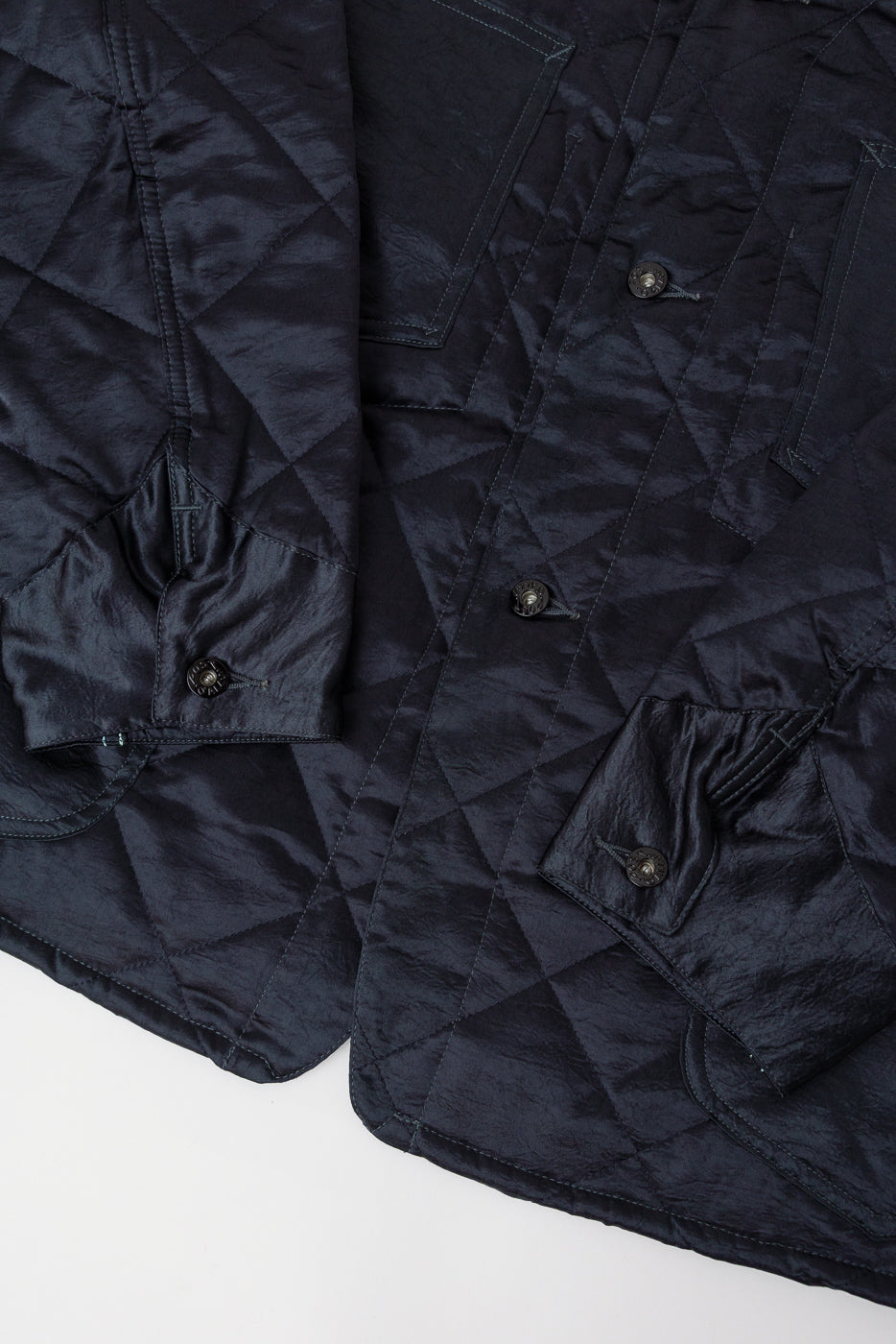Close-up of front body and sleeve of dark grey quilted acetate sateen coverall, highlighting pocket, buttons, and fabric texture.