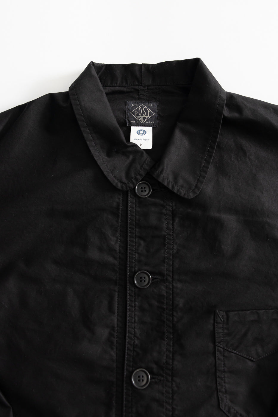 Close-up of front upper chest and collar of a black moleskin shirt, showing buttons, chest pocket, and tag details.
