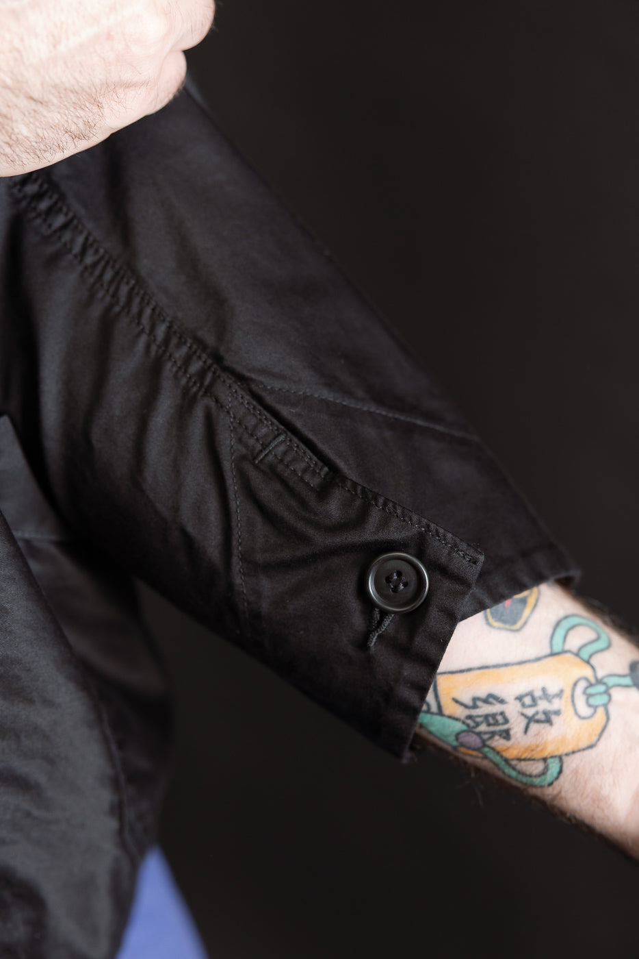 Close-up of male model's forearm showing black moleskin shirt sleeve cuff, button detail, and visible fabric texture; model is 5'9