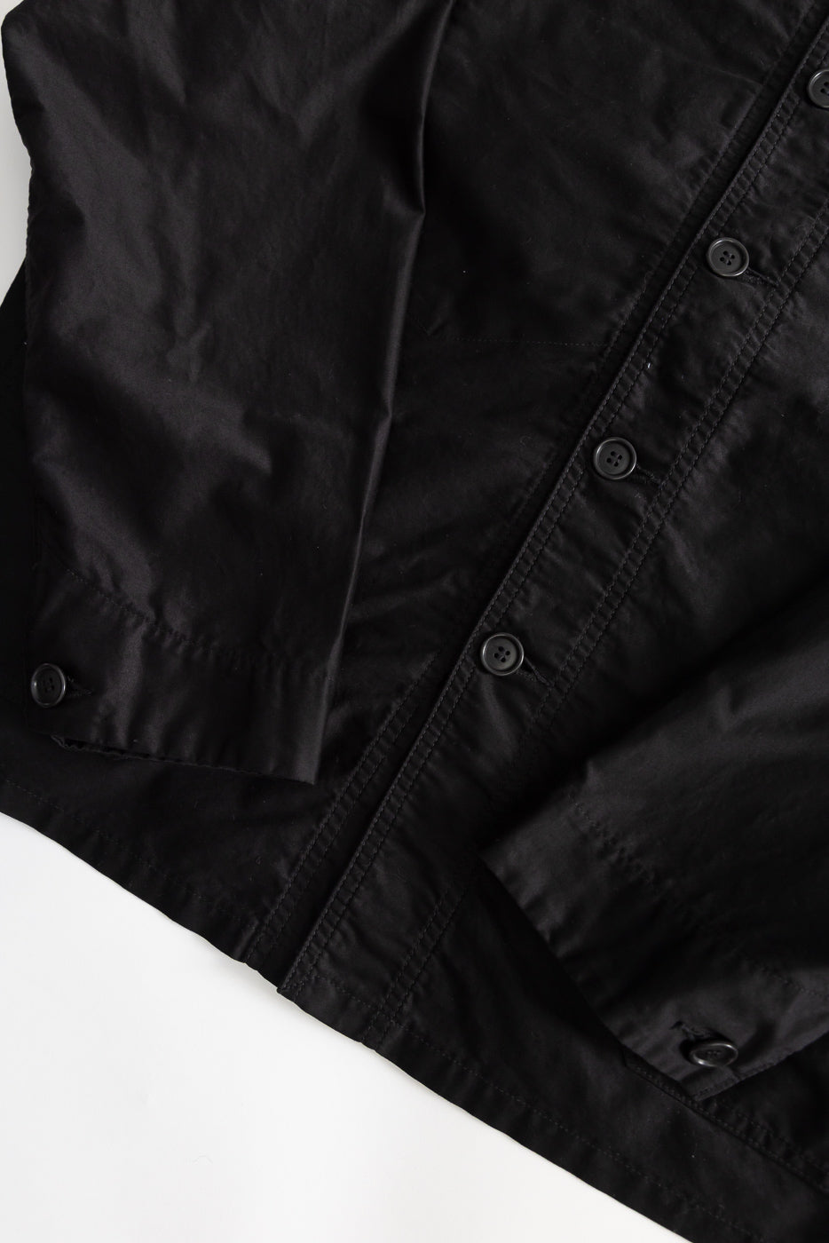 Close-up of front left side of black moleskin jacket, showing buttons, cuff, and fabric texture.
