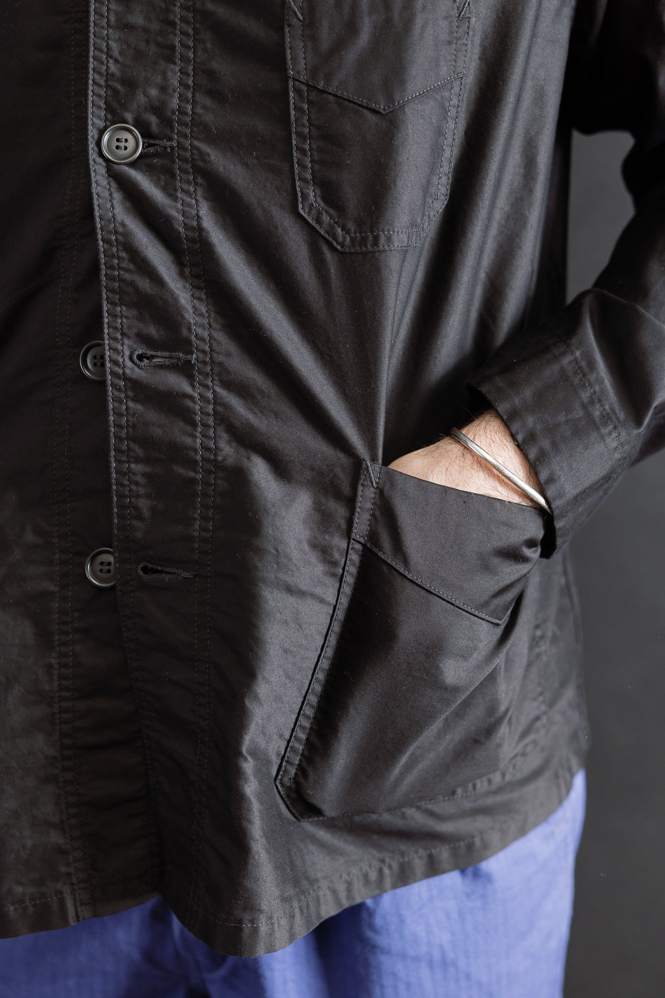 Close-up of front left side of black moleskin work jacket, male model hand in pocket, showing buttons and pocket details, model is 5'9
