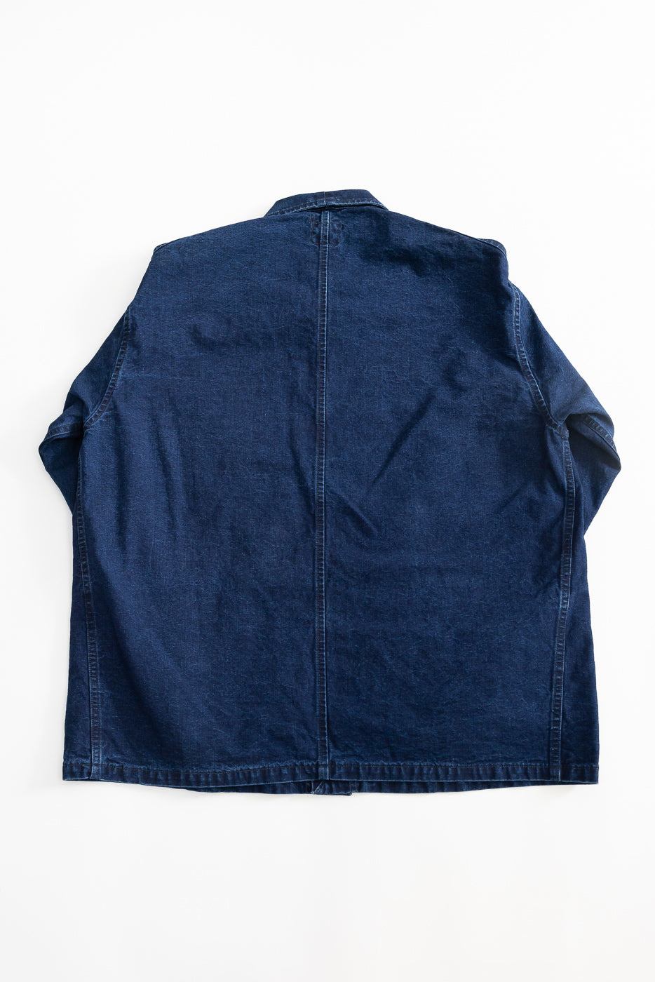 Flat lay of indigo canvas chore jacket, back view showing seam details and straight hem.
