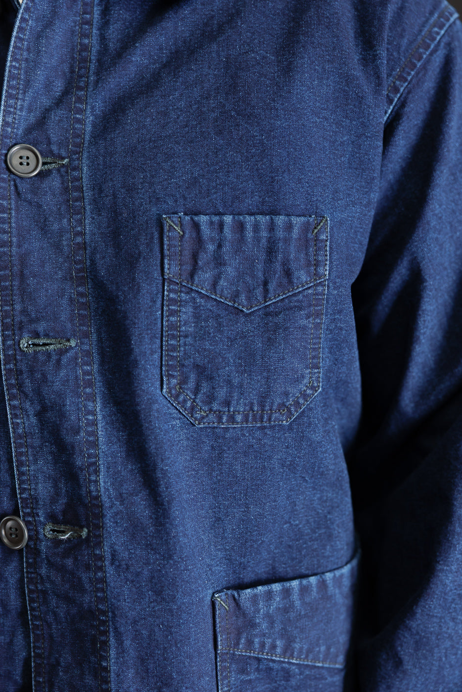 Close-up of front left chest and waist pockets on indigo canvas work jacket, highlighting pocket stitching and button details.