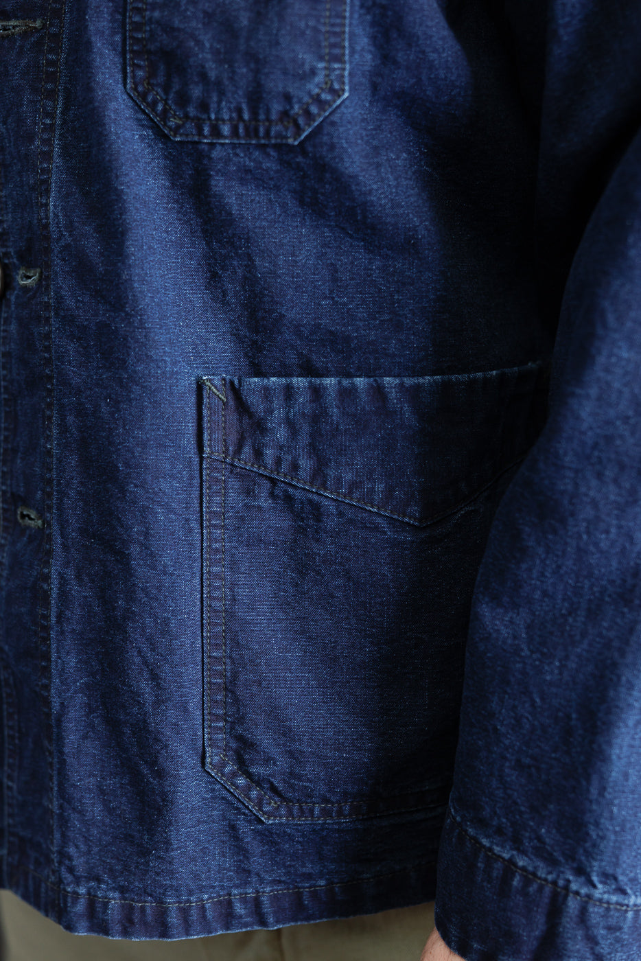 Close-up of male model's front left side, showing indigo canvas work jacket pocket and fabric texture.
