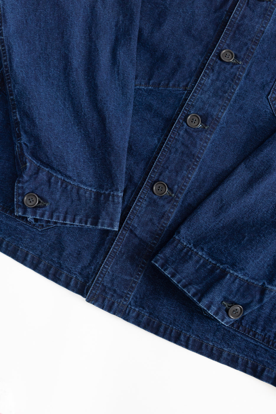Close-up of front torso and sleeves of deep washed indigo canvas chore jacket, showing button details and pocket stitching.