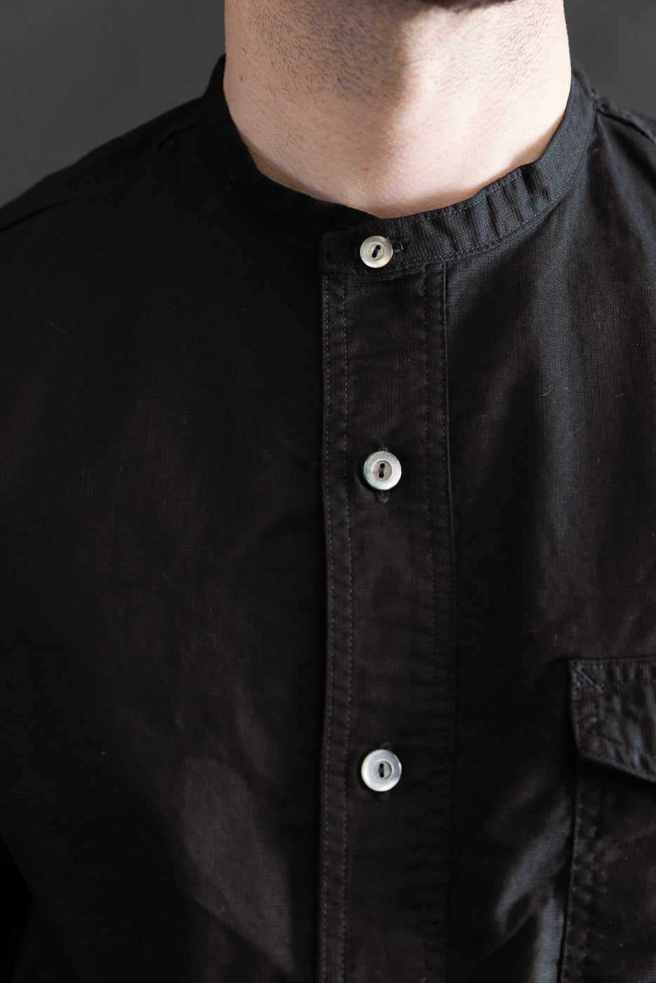 Close-up of front chest and collar of men's black band collar shirt, showing buttons and chest pocket, modeled by male 5'9