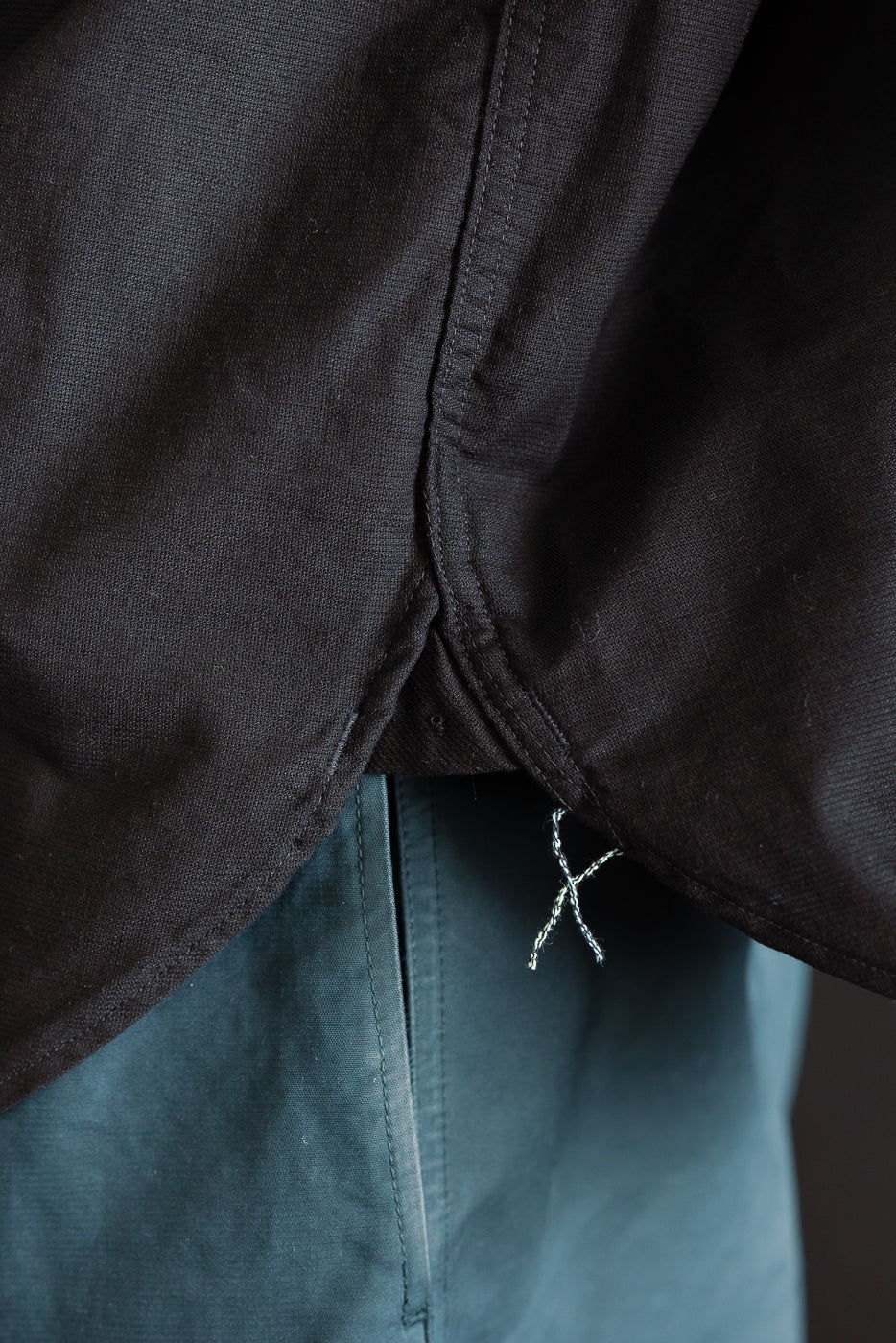 Close-up of black shirt hem detail and stitching, side view, fabric texture visible