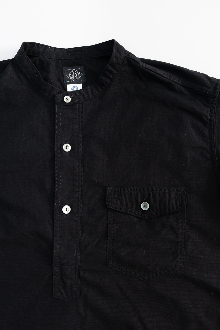 Close-up front view of black band collar short sleeve shirt, showing buttons and chest pocket.