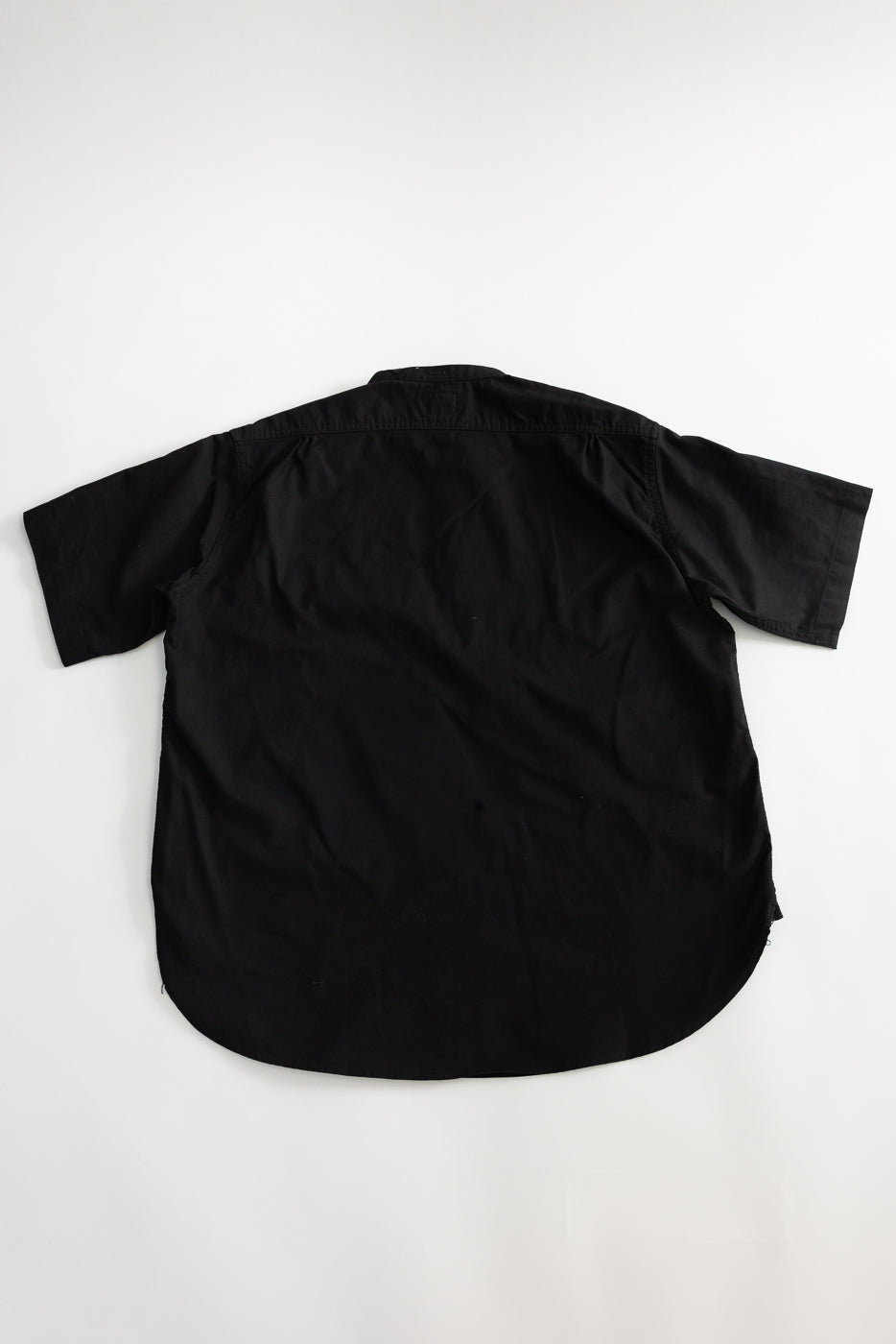 Flat lay of black short sleeve shirt, back view, showing fabric texture and straight hem.