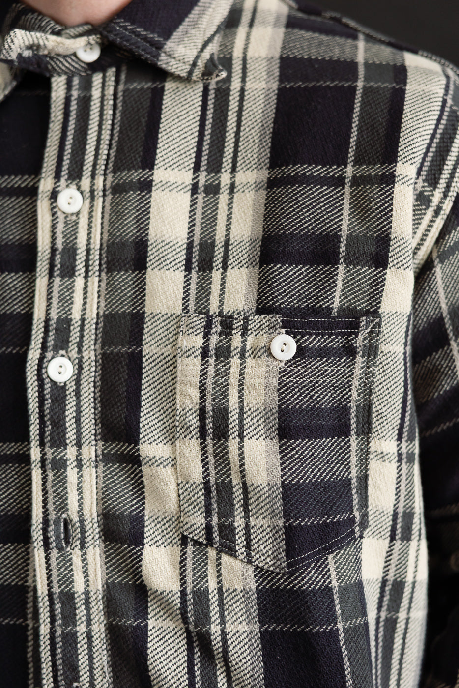 Close-up of front chest pocket on Post O'Alls St. Louis grey plaid flannel shirt, showing white buttons, button-down collar, and soft cotton fabric texture, male model 5'9