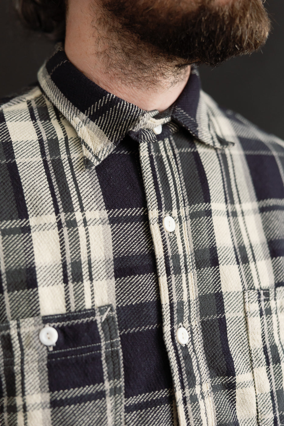 Close-up front view of men's Post O'Alls St. Louis grey plaid cotton flannel shirt collar, buttons, and chest pocket on male model, 5'9